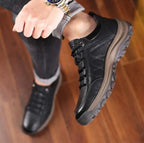 Close-up of black leather shoe worn on foot, paired with grey turned-up trousers