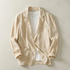 Beige linen blazer laid flat open over a white tee, highlighting natural woven texture and patch pockets