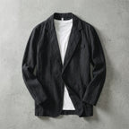 Black linen blazer laid flat buttoned over a white t-shirt, showing clean lapel and twin patch pockets