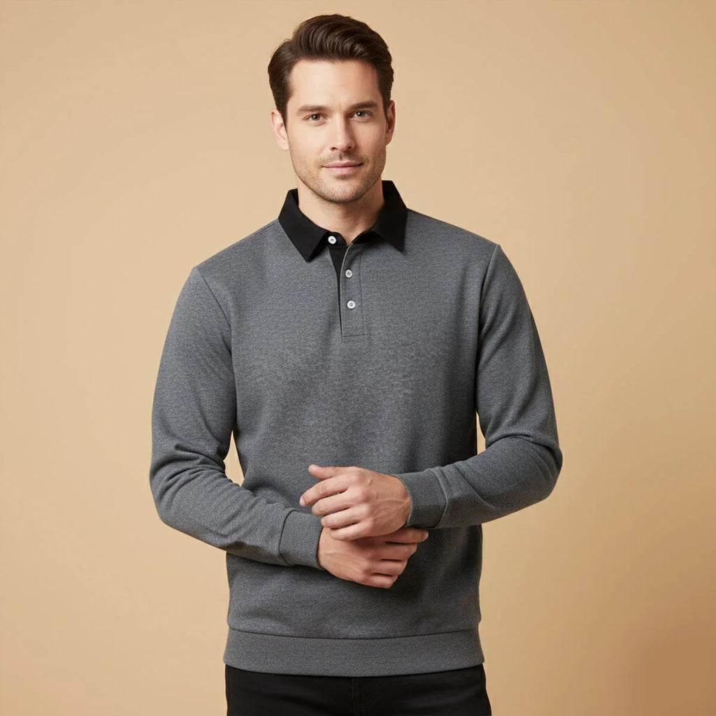 Man wearing a dark grey marl long sleeve polo jumper with black collar against a neutral tan backdrop