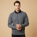 Man wearing a dark grey marl long sleeve polo jumper with black collar against a neutral tan backdrop