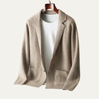 Beige knitted blazer-style cardigan with notch lapel and patch pockets, shown on a wooden hanger over a white tee