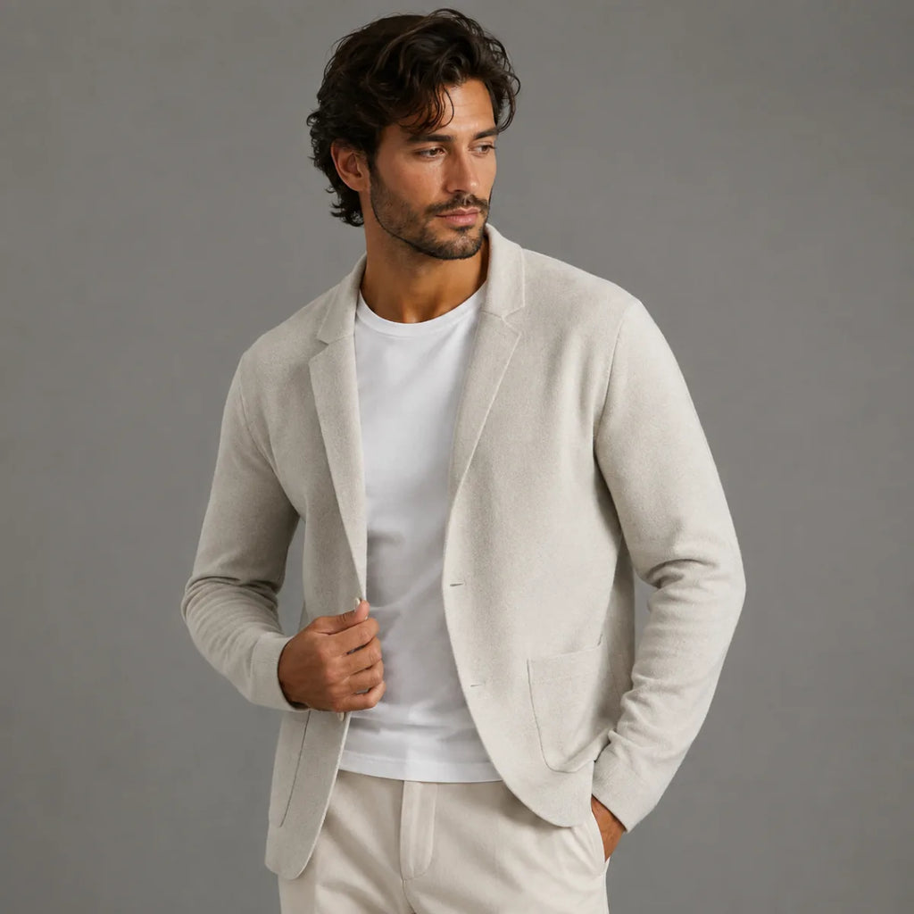 Man wearing a light grey knit blazer cardigan open over a white t-shirt, one hand holding the lapel