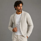 Man wearing a light grey knit blazer cardigan open over a white t-shirt, one hand holding the lapel