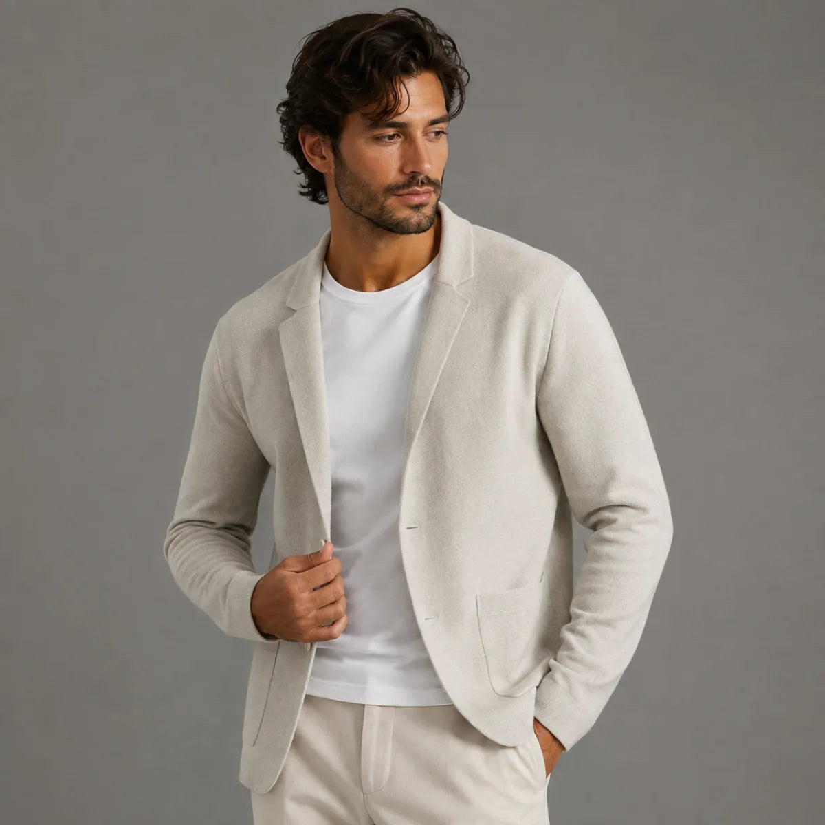 Man wearing a light grey knit blazer cardigan open over a white t-shirt, one hand holding the lapel