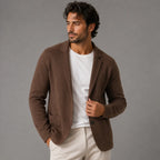 Man wearing a brown knitted blazer cardigan open over a white t-shirt and cream trousers, holding the lapel