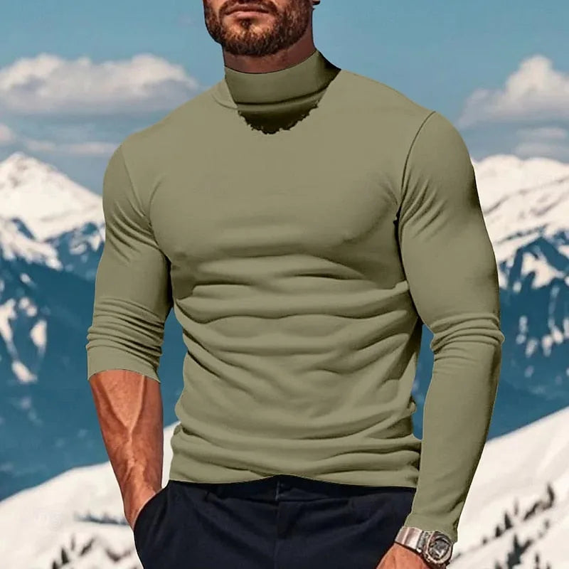 Man modelling a light green mock neck top with fitted sleeves and ribbed collar, mountain scenery behind
