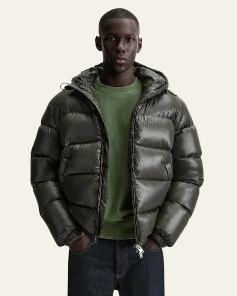 Man wearing an olive green glossy puffer jacket open over a green jumper and jeans