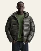 Man wearing an olive green glossy puffer jacket open over a green jumper and jeans