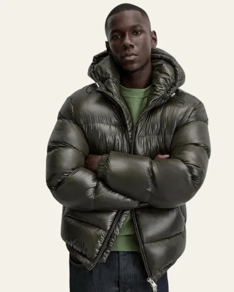 Man with arms crossed wearing the olive green puffer jacket with hood raised