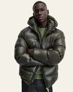 Man with arms crossed wearing the olive green puffer jacket with hood raised
