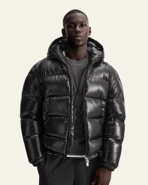 Front view of a man wearing the black glossy puffer jacket unzipped over a grey jumper
