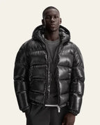 Front view of a man wearing the black glossy puffer jacket unzipped over a grey jumper