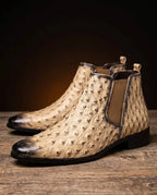 Close-up side view of beige Chelsea boots with ostrich-embossed leather texture, dark burnished toe and tan elastic side panel