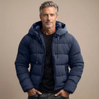 Man wearing a navy quilted puffer jacket with hood, drawstrings and zip pockets, worn open over a black t-shirt