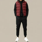 Man wearing a burgundy quilted gilet zipped over a black hoodie, paired with black joggers and white trainers