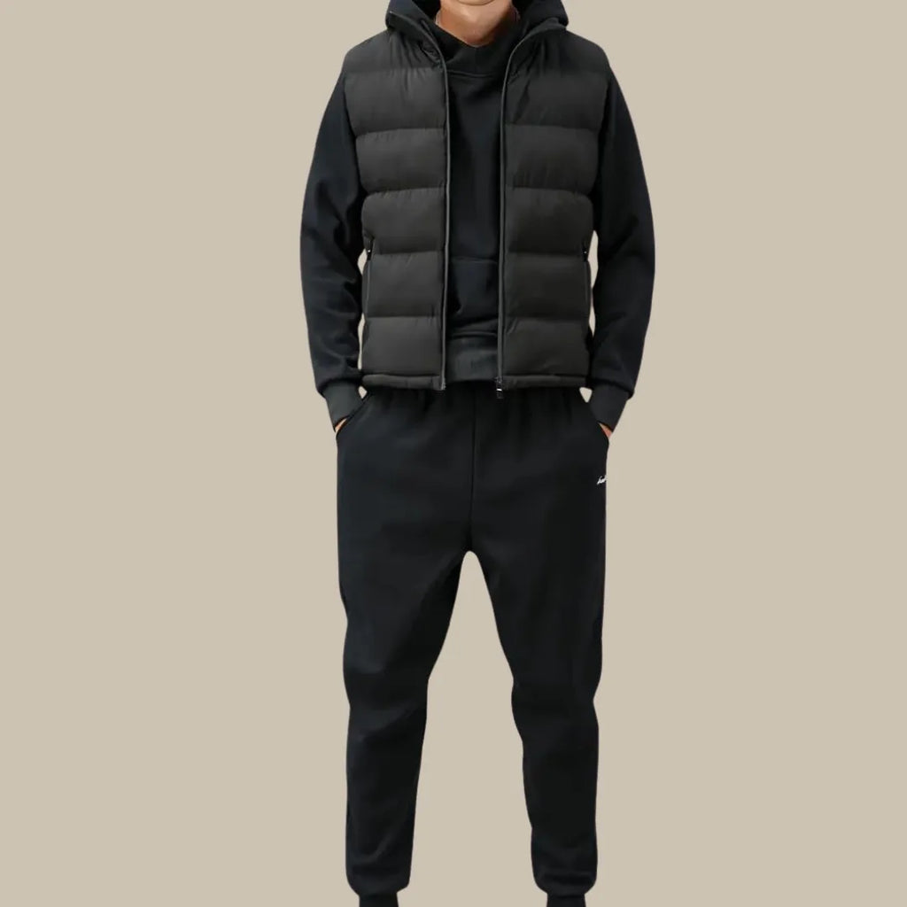 Man wearing a black quilted gilet zipped over a black hoodie, styled with black joggers for a casual look