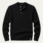 Flat lay of a black ribbed knit henley jumper with three-button placket and leather brand tab on the hem