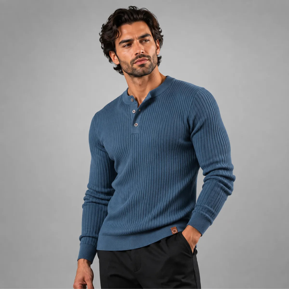 Man wearing a slate blue ribbed henley jumper with hand in pocket, paired with black trousers