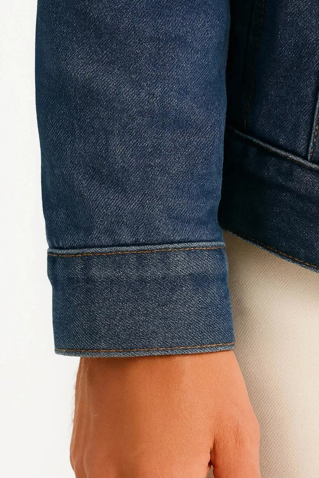 Close-up of the buttoned cuff and fold-back hem on the dark denim sleeve