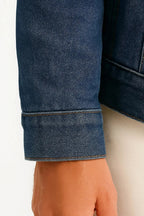 Close-up of the buttoned cuff and fold-back hem on the dark denim sleeve