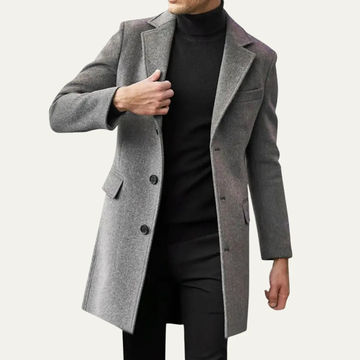 Man wearing a grey overcoat open over a black polo neck and trousers, adjusting the lapel