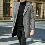 Side view of a man walking outdoors in a grey wool overcoat over a black polo neck jumper