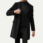Man wearing a black single-breasted overcoat over a black polo neck, buttoned at the front