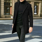 Man walking on a city street wearing an open black wool overcoat over black trousers
