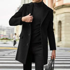 Close-up of a man adjusting the lapel of a black wool overcoat, holding a bag, street background