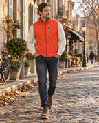 Side view of an orange softshell gilet worn over a cream knit jumper with dark jeans and brown suede boots.