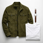 Flat lay of the folded olive suede jacket beside a white t-shirt and a brown leather strap watch