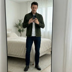 Man taking a mirror selfie in an olive suede jacket paired with a white tee, dark jeans and ankle boots