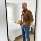 Man taking a mirror selfie in a tan suede jacket layered over a white t-shirt with light wash jeans