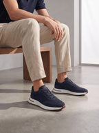 Man seated on a wooden bench wearing navy suede trainers with mesh panels and white chunky soles