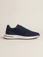 Side profile of a navy suede trainer with mesh overlay on a plain stone background