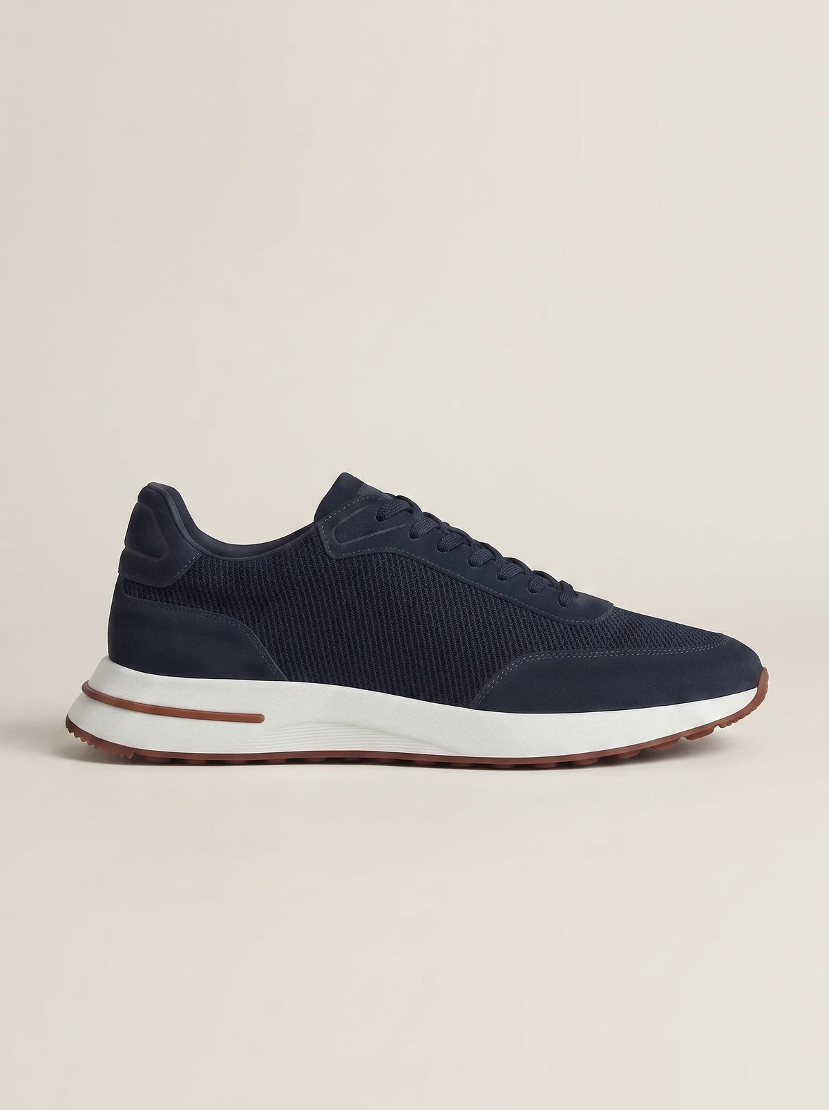 Side profile of a navy suede trainer with mesh overlay on a plain stone background