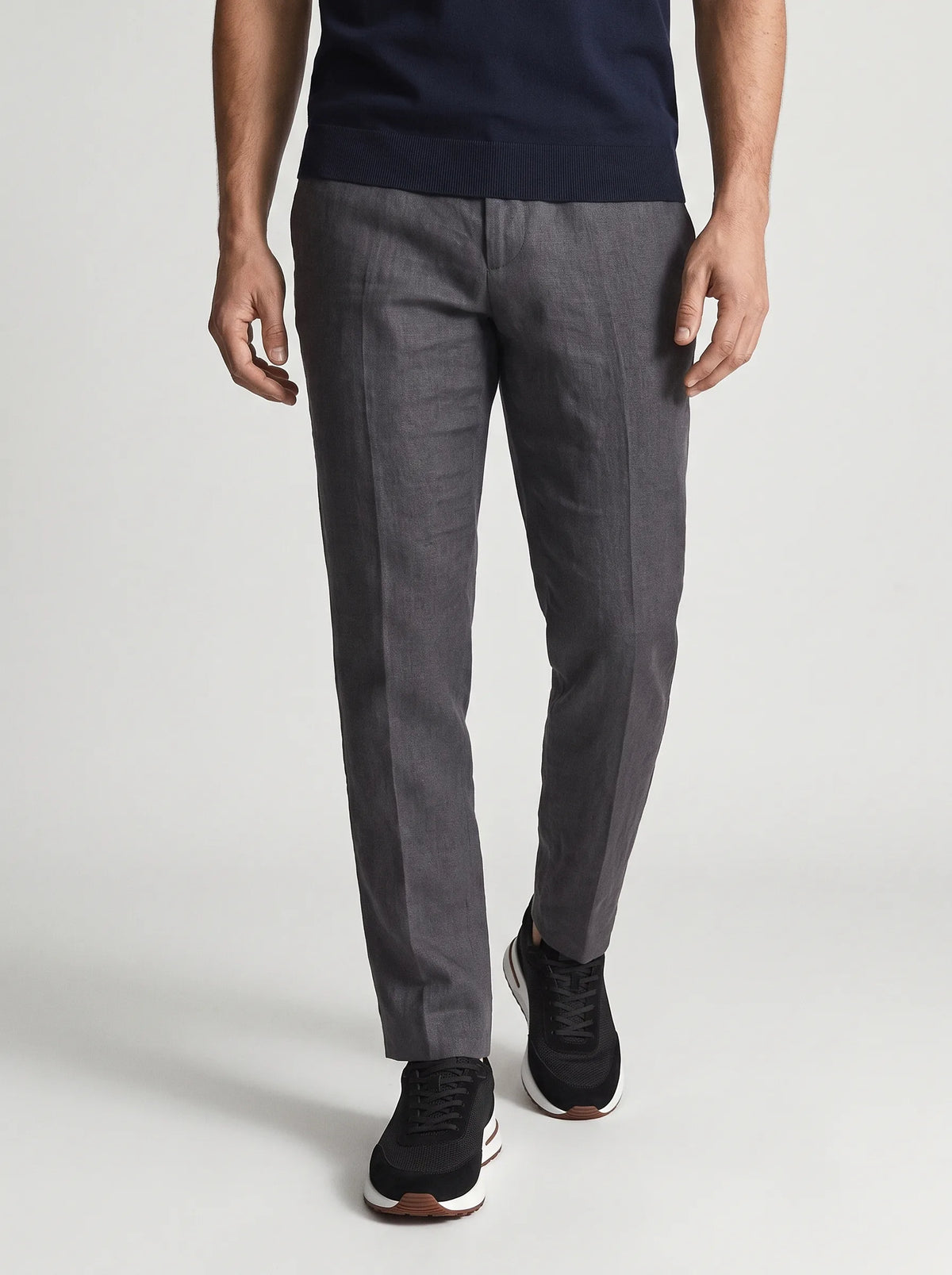 Man walking in grey linen trousers wearing black suede trainers with white midsole and brown trim