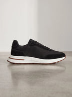 Side profile of a black suede trainer with mesh panel, white midsole and brown stripe detail on a concrete floor