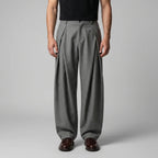 Front view of grey tailored wide-leg trousers with deep pleats, worn with a black T-shirt and brown leather shoes