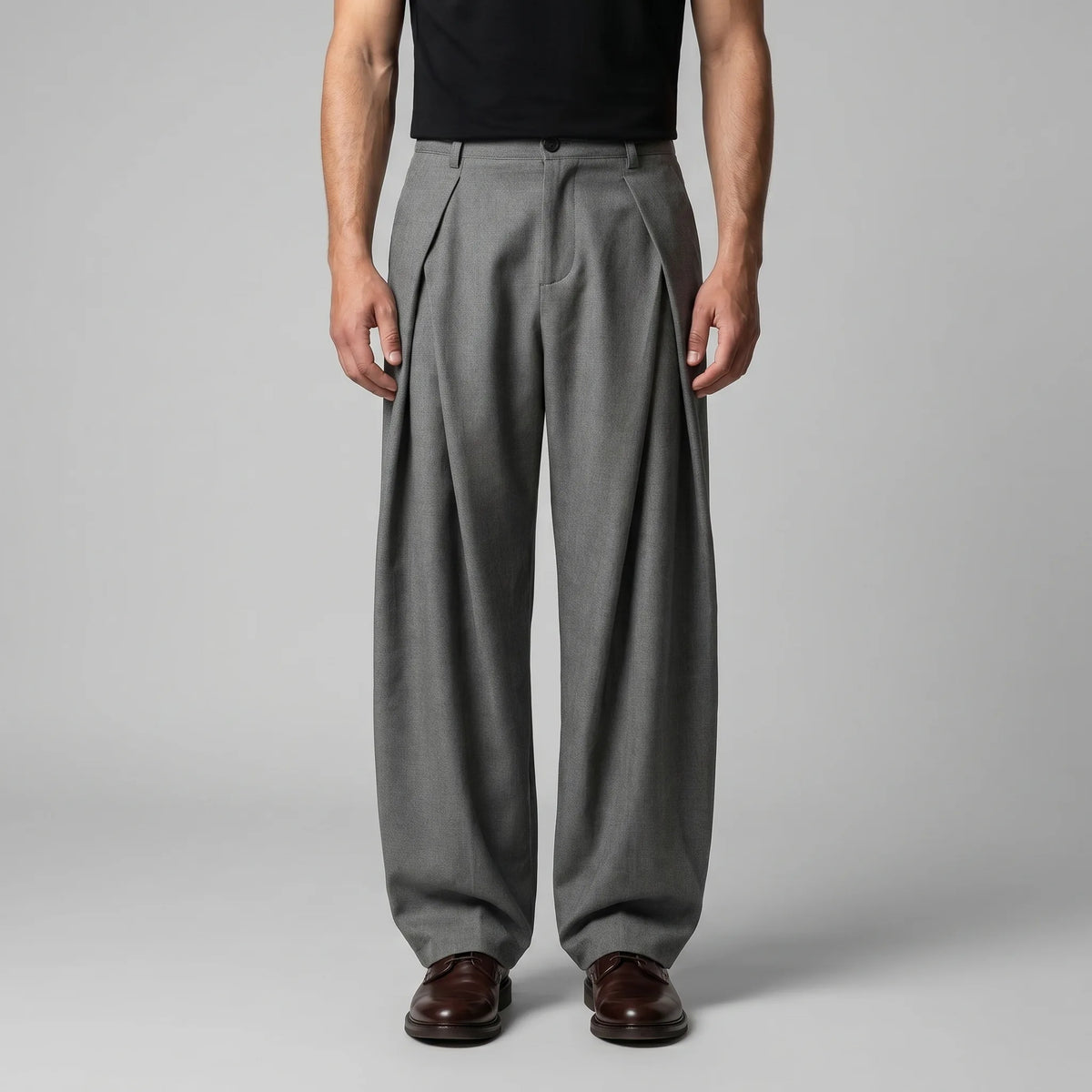 Front view of grey tailored wide-leg trousers with deep pleats, worn with a black T-shirt and brown leather shoes