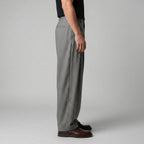 Side profile showing the relaxed, sculpted drape of the grey wide-leg trousers from waist to hem