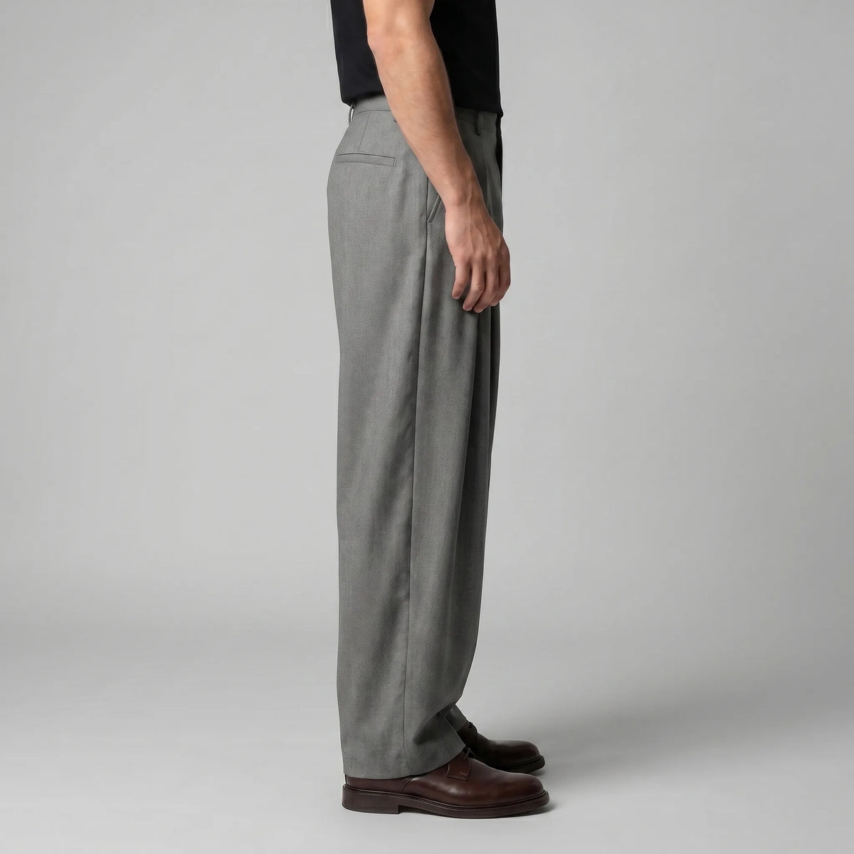 Side profile showing the relaxed, sculpted drape of the grey wide-leg trousers from waist to hem