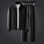 Black zip-up tracksuit jacket and trousers with white side stripes displayed on hangers against a dark grey backdrop