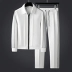 White zip-up tracksuit jacket and trousers with black side stripes shown together on hangers against a dark grey backdrop