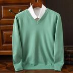 Sage green V-neck jumper with ribbed collar layered over a white shirt, displayed on a wooden hanger