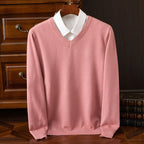 Dusty pink V-neck jumper layered over a white shirt collar, styled on a hanger near stacked books