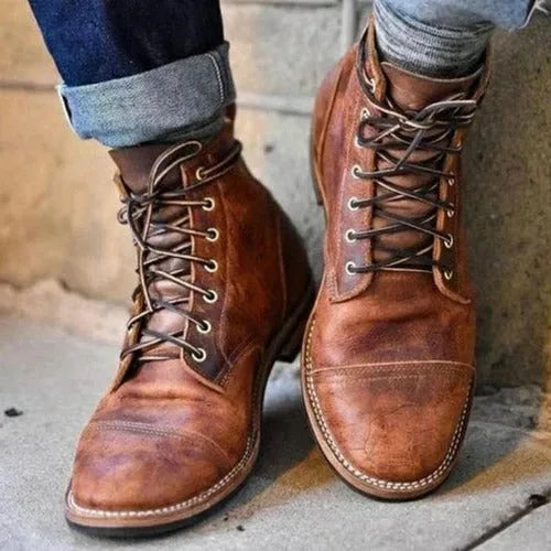 Close-up of rugged tan leather lace-up boots with cap toe, worn with cuffed dark denim jeans