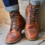 Close-up of rugged tan leather lace-up boots with cap toe, worn with cuffed dark denim jeans