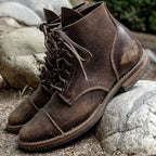 Pair of weathered dark brown leather lace-up boots with cap toe resting on stone outdoors